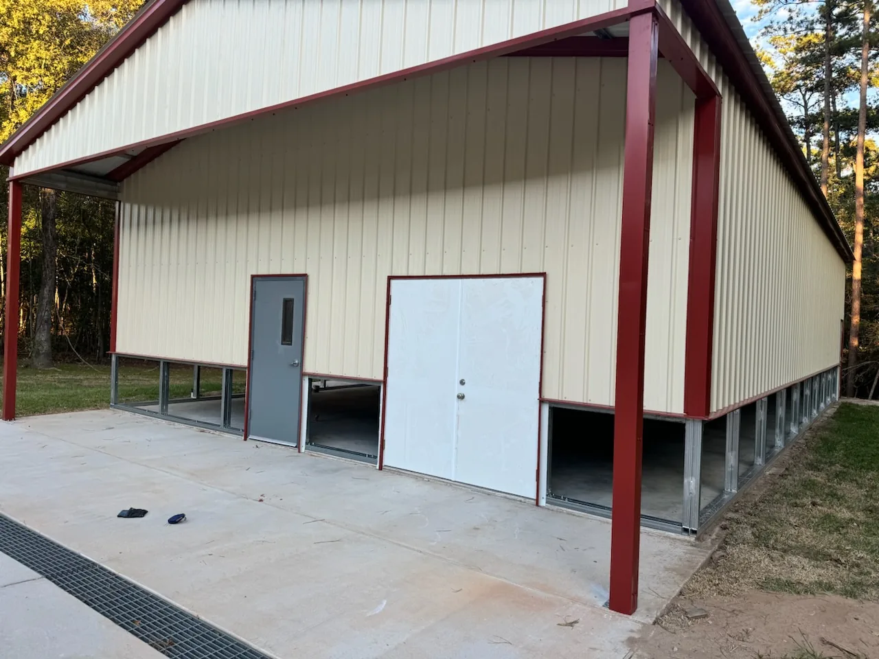 Light-colored metal building with exposed red framing and a covered front edge